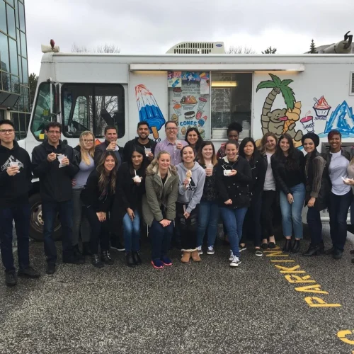 A group of employees posing happily near an ice cream truck during a corporate event.