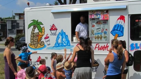 A group of children with adults gathered near an ice cream truck, excitedly waiting for their turn during a birthday party.