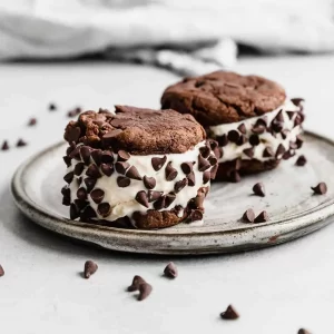 Chocolate chip ice cream sandwiches with chocolate cookies on a rustic plate.